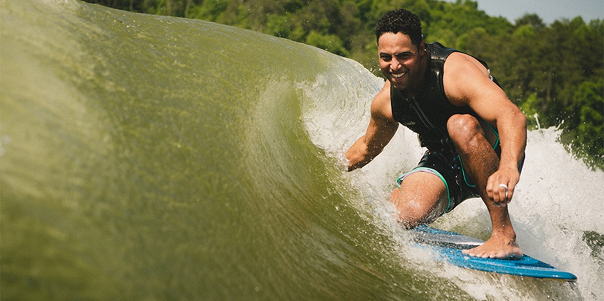 A surfer puts his hand in the wave behind an XT wake boat