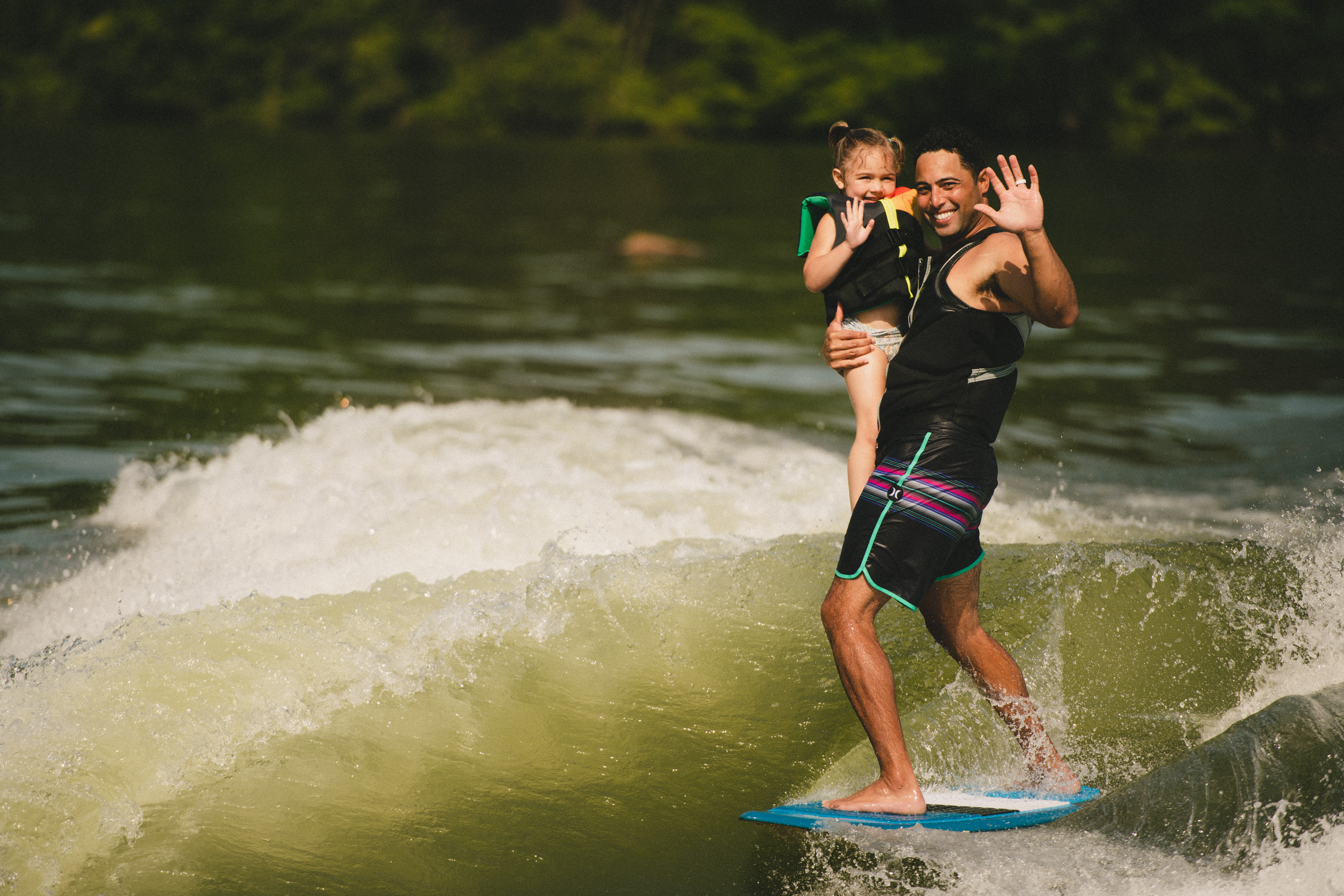 A surfer holds up a little girl while riding a wave
