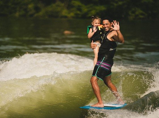 A surfer holds up a little girl while riding a wave